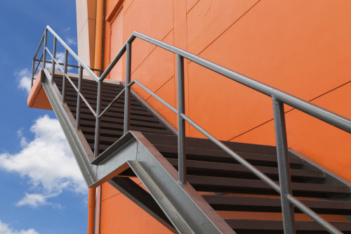 Metal fire escape or emergency exit on Orange Wall of Building With Blue Sky and White Cloud